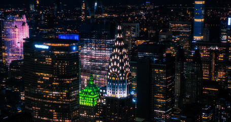 Aerial Night Scenery Over Manhattan Downtown Business Area. Close Up Arc Shot of the Rooftop Tower of the Art Deco Office Building with Lights Working in the Windows on the Rooftop Spire