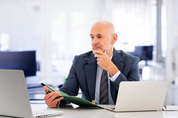 A middle-aged businessman sitting at his desk in the office and having video conference