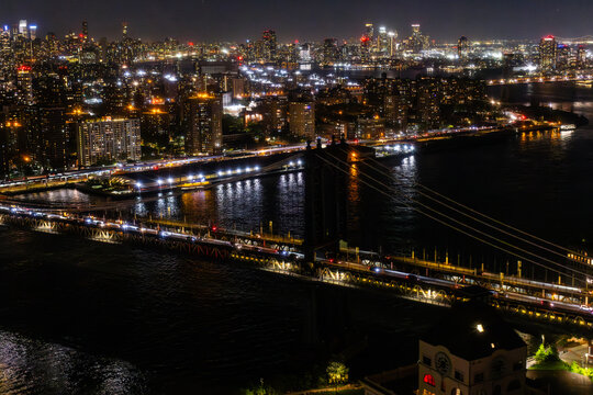 New York City Skyline Aerial Photo from a Helicopter at Night. Famous Skyscraper Buildings with Manhattan Bridge. Busy Diverse Megapolis with Cars, Boats and People Moving Around