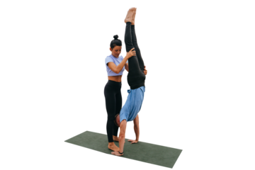 Female fitness trainer helps young man to do handstand against transparent background on exercise  by holding guy's legs. Training outside, healthy lifestyle. Couple training together.