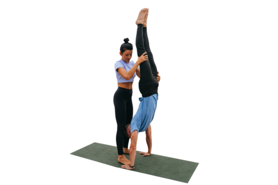Female fitness trainer helps young man to do handstand against transparent background on exercise  by holding guy's legs. Training outside, healthy lifestyle. Couple training together.