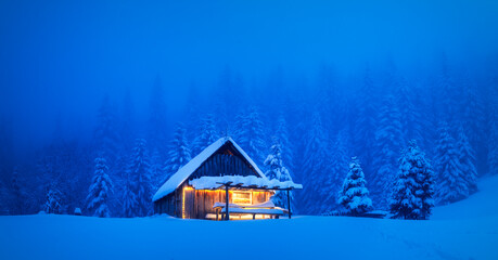 A serene winter scene with a lonesome wooden house and snow-draped conifers on a mountain glade in...