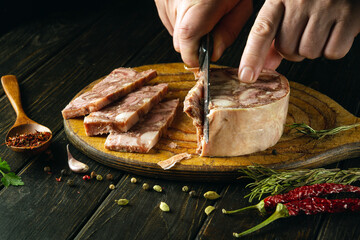 Close-up of a man with a knife in his hand cutting headcheese on the kitchen table to prepare the Belgian national dish. Peasant food