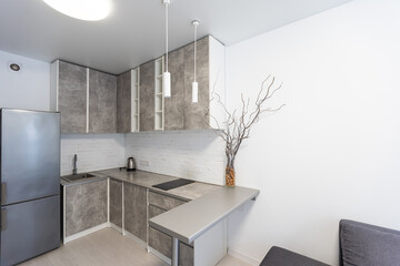 Spacious kitchen with minimalist square shaped furniture, grey floor and walls, counter with...