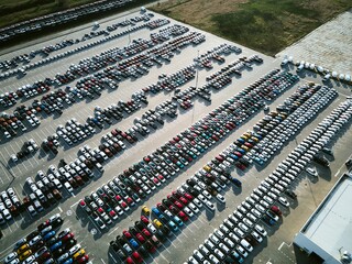 Aerial view of a massive parking lot at a car manufacturing facility with newly produced vehicles parked in rows.
