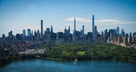 Fototapeta na wymiar Sunny Weather New York City Aerial Landscape Over Central Park with Midtown Manhattan Skyscrapers. Cinematic Drone View of Urban Skyline with Slightly Cloudy Blue Sky