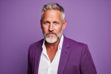 Portrait of a handsome mature man with grey beard and mustache wearing purple suit and looking at...