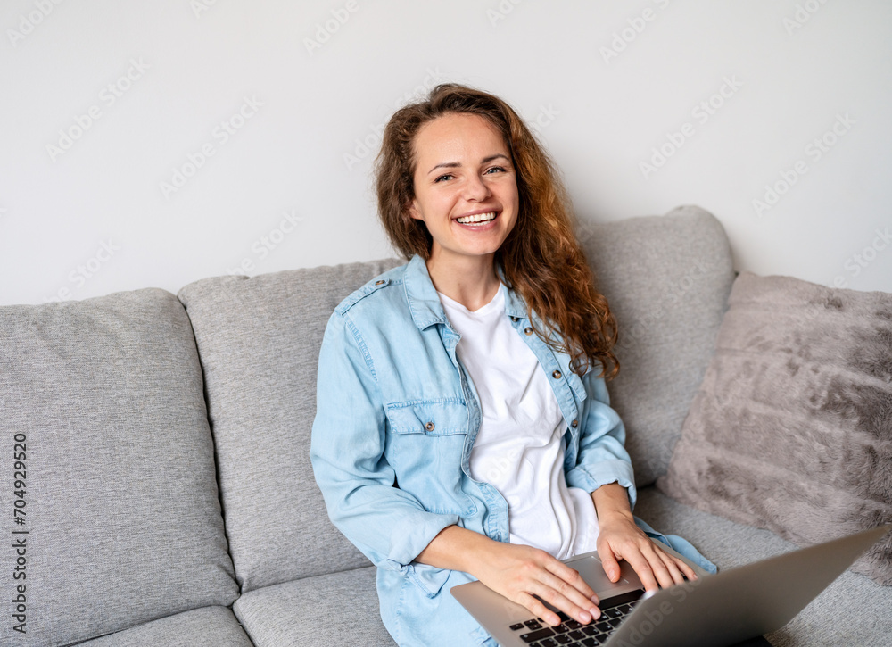 Wall mural happy young brunette woman caucasian ethnicity sits on the sofa at home and using her laptop compute