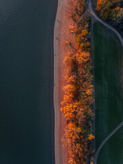 Top view of lake shore, surrounded by autumn forest with sand coastline, beach.