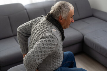 Elderly man near sofa with cactus at home. Hemorrhoids concept - obrazy, fototapety, plakaty