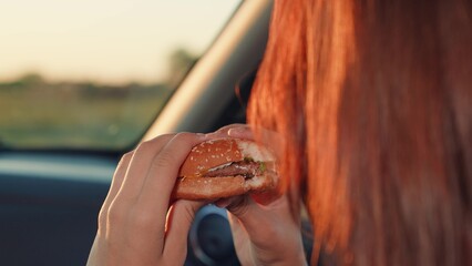 young girl eats hamburger while sitting car seat, girl face touches hamburger close-up, trip...
