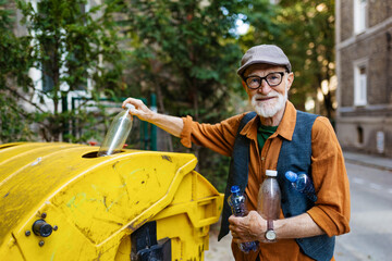 Senior man throwing plastic waste, bottles into recycling container in front apartment. Elderly man sorting the waste according to material into colored bins.