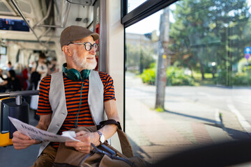 Elderly man traveling through the city by bus, reading newspaper. Senior city commuter taking tram...