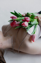 Beautiful young sexy girl in a white top and black pants with an open neckline with a beautiful spring bouquet of pink-red tulips, a holiday gift for a woman
