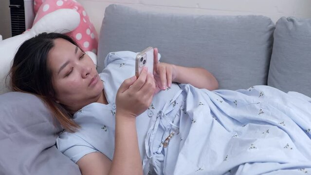 Reading some messages and checking her social media while lying on her couch in her living room.