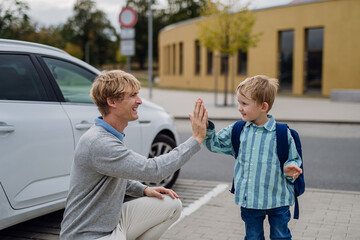 Father saying goodbyeto to son in front of school building, high five each other. Dad heading to...