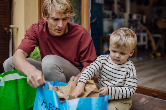 Father teaching son recycle waste. Boy sorting the waste according to material into colored bags.