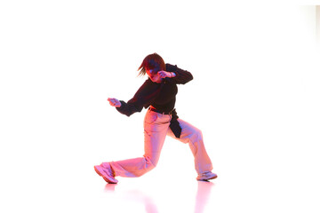 Young artistic woman in casual outfit dancing, performing hip hop isolated over white background in neon light. Concept of contemporary dance, street style, youth, hobby, action, lifestyle