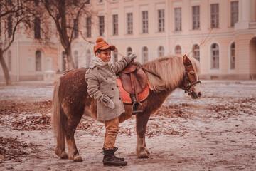 smiling boy stands next to a pony holding the pommel of the saddle