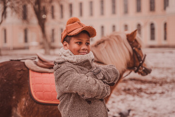 smiling boy with his arms folded on his chest against the background of a pony