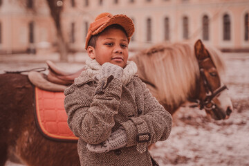 a thoughtful boy rests his chin on his fist against the background of a pony