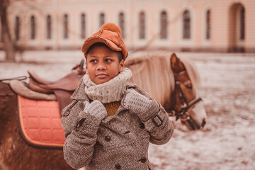 a serious boy thoughtfully pulls his coat collar against the background of a pony