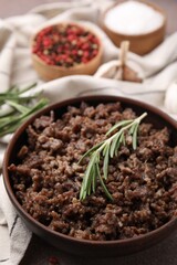 Fried ground meat in bowl and rosemary on table, closeup