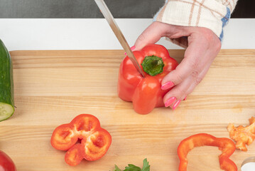 Removing the stem from a sweet pepper pod with a knife on a wooden cutting board.