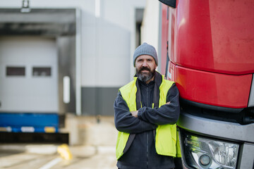 Truck driver standing with arms crossed leaning on red truck and looking at camera. © Halfpoint