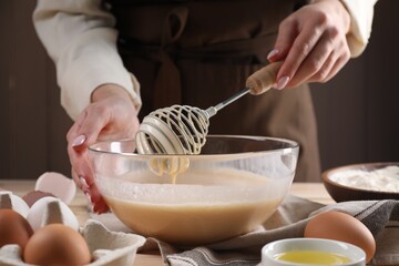 Woman making dough with whisk in bowl at table, closeup