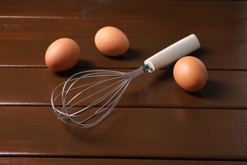 Metal whisk and raw eggs on wooden table, closeup