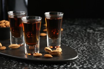 Glasses with tasty amaretto liqueur and almonds served on black table, closeup. Space for text