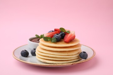 Delicious pancakes with strawberries, blueberries, and chocolate sauce on pink background, closeup