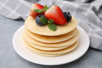 Stack of tasty pancakes with fresh berries, mint and honey on light grey table, closeup