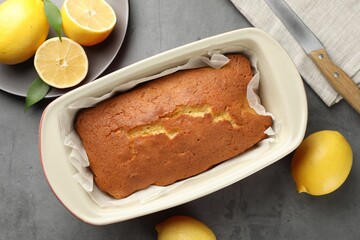 Tasty lemon cake in baking dish and citrus fruits on grey table, flat lay
