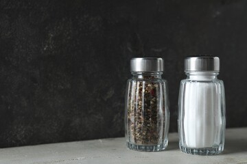 Salt and pepper shakers on light table against grey background, closeup. Space for text