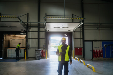 Warehouse receiver overseeing the storing of delivered items, holding tablet, looking at cargo...