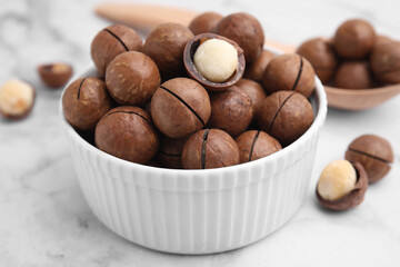 Tasty Macadamia nuts in bowl on white table, closeup