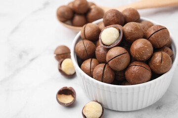Tasty Macadamia nuts in bowl on white marble table, closeup. Space for text