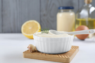 Fresh mayonnaise sauce in bowl and ingredients on white table