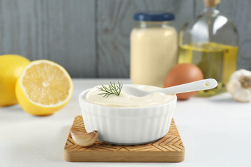Fresh mayonnaise sauce in bowl and ingredients on white table