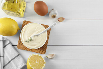 Fresh mayonnaise sauce in bowl and ingredients on white wooden table, flat lay. Space for text