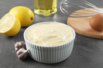 Fresh mayonnaise sauce in bowl and ingredients on grey table