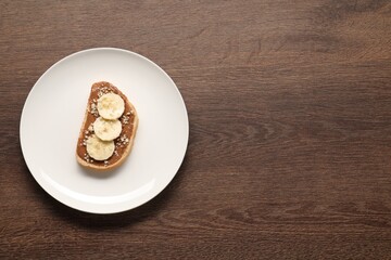 Toast with peanut butter, banana slices and nuts on wooden table, top view. Space for text