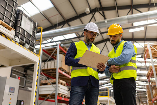 Engineer consulting with foreman in modern industrial factory, talking about new production project or investment. Team management in manufacturing facility.