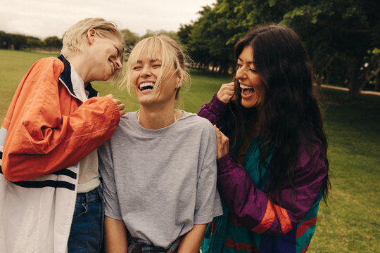 Three female friends laughing and bonding outdoors in a casual park hangout