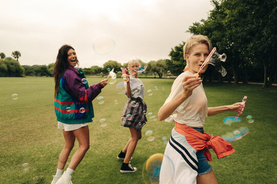 Three friends blowing bubbles in a celebration of summer in the park