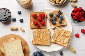 Delicious toasts with peanut butter, raspberries, blueberries and nuts on white tiled table, flat...