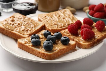 Delicious toasts with peanut butter, raspberries and blueberries on white table, closeup