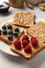 Delicious toasts with peanut butter, raspberries and blueberries on white table